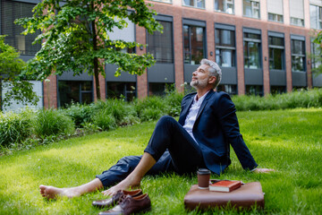 Mature businessman resting and sitting barefoot in park, feeling free, escaping from work, work life balance concept.