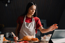 Young Hispanic Woman Using Tablet-computer While Cooking In Kitchen