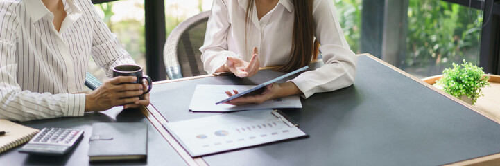 Wall Mural - Coworker business concept, Two businesswoman reading report on tablet to discussing new project