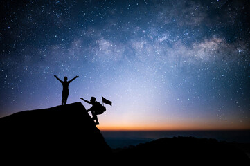 Wall Mural - Two young tourist with backpack is climbing a cliff with beautiful night sky, Milky Way and star over the sky. He had an effort to climb all the way to the top of the mountain and he had to succeed.