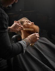 Wall Mural - Getting perfect beard's shape. Close-up of young bearded man getting beard haircut by hairdresser or barber at barbershop.