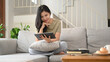 © Prathankarnpap - Smiling young asian woman in casual clothes using digital tablet on couch in cozy living room