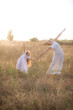 © capable97 - A cute little girl with long blond curly hair and her mother in a white summer dress and a straw boater hat in a field in the countryside in summer at sunset. Nature and Ecolife