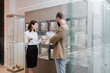 © LIGHTFIELD STUDIOS - Smiling seller pointing with hands near showcases and customer in jewelry shop.
