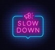 Slow Down neon sign in the speech bubble on brick wall background.