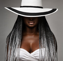 Wall Mural - African Woman with Long Braids Hair. Black and White Concept. Beauty Model in Big Hat hidden Face. Afro Hairstyle and Lips Makeup. Sexy Mysterious Women Portrait over Gray Studio Background