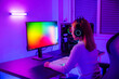 Leinwandbild Motiv Asian professional gamer playing online video game on desktop computer PC have colorful neon LED lights, young woman in gaming headphones using computer for playing game at home