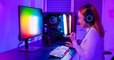 Winning Victory. Asian gamer playing online video game excited on desktop computer PC colorful neon LED lights, woman in gaming headphones use computer she happy successful, E-Sport concept, side view