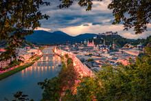 Illuminated Streets In Salzburg Town. Aerial Summer View Of Old City, Birthplace Of Famed Composer Mozart And Salzach River. Gloomy Sunset In Eastern AlpsAustria, Europe. Traveling Concept Background.