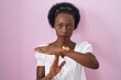 African woman with curly hair standing over pink background doing time out gesture with hands, frustrated and serious face