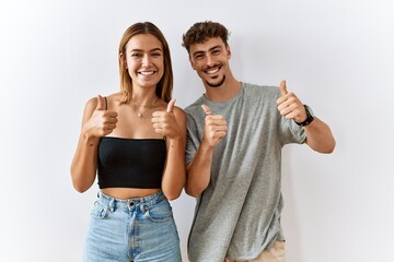 Poster - Young beautiful couple standing together over isolated background success sign doing positive gesture with hand, thumbs up smiling and happy. cheerful expression and winner gesture.