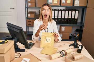 Wall Mural - Young blonde woman working at small business ecommerce afraid and shocked with surprise and amazed expression, fear and excited face.