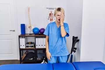 Wall Mural - Young physiotherapist woman working at pain recovery clinic yawning tired covering half face, eye and mouth with hand. face hurts in pain.