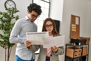 Two business workers with serious expression reading paperwork working at the office.