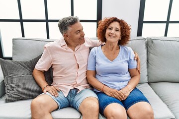 Poster - Middle age man and woman couple smiling confident hugging each other sitting on sofa at home