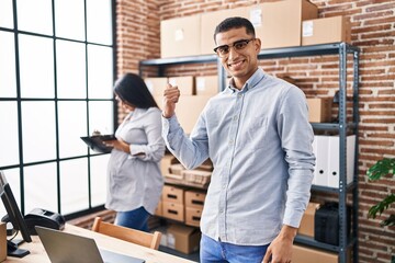 Young hispanic couple expecting a baby working at small business ecommerce smiling happy pointing with hand and finger to the side