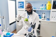 African American Man Working At Scientist Laboratory With Apple Skeptic And Nervous, Frowning Upset Because Of Problem. Negative Person.