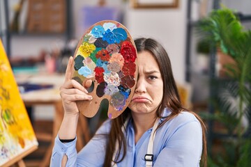 Canvas Print - Young brunette woman covering face with painter palette depressed and worry for distress, crying angry and afraid. sad expression.