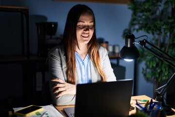 Poster - Young brunette woman working at the office at night happy face smiling with crossed arms looking at the camera. positive person.