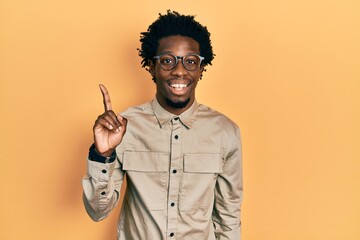 Wall Mural - Young african american man wearing casual clothes and glasses showing and pointing up with finger number one while smiling confident and happy.