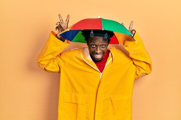 Sticker - Young african american man wearing yellow raincoat posing funny and crazy with fingers on head as bunny ears, smiling cheerful