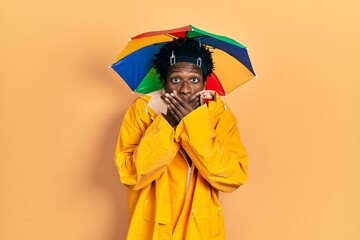 Wall Mural - Young african american man wearing yellow raincoat shocked covering mouth with hands for mistake. secret concept.