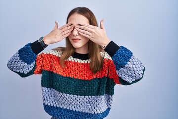 Poster - Young hispanic girl standing over blue background covering eyes with hands smiling cheerful and funny. blind concept.