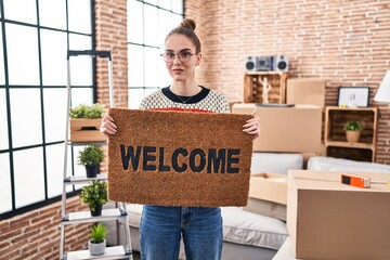 Canvas Print - Young hispanic girl holding welcome doormat relaxed with serious expression on face. simple and natural looking at the camera.