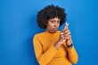 © Krakenimages.com - Black woman with curly hair standing over blue background holding symbolic gun with hand gesture, playing killing shooting weapons, angry face