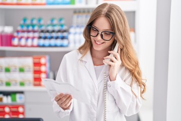 Canvas Print - Young woman pharmacist talking on telephone reading prescription at pharmacy