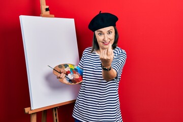 Wall Mural - Middle age hispanic woman standing drawing with palette by painter easel stand beckoning come here gesture with hand inviting welcoming happy and smiling