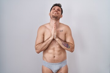 Young hispanic man standing shirtless wearing underware begging and praying with hands together with hope expression on face very emotional and worried. begging.