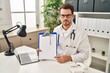 © Krakenimages.com - Young hispanic man wearing doctor stethoscope holding clipboard thinking attitude and sober expression looking self confident
