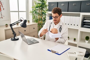 Sticker - Young hispanic man wearing doctor uniform having video call holding brain at clinic