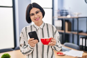 Wall Mural - Young chinese woman business worker using smartphone and drinking coffee at office