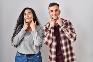 Wall Mural - Young hispanic couple standing over white background smiling with open mouth, fingers pointing and forcing cheerful smile