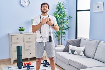 Wall Mural - Handsome latin man wearing sportswear at home smiling with hands on chest with closed eyes and grateful gesture on face. health concept.