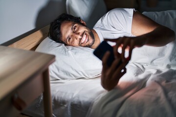 Sticker - Young hispanic man using smartphone lying on bed at bedroom