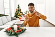 © Krakenimages.com - Arab young man sitting on the table by christmas tree smiling looking to the camera showing fingers doing victory sign. number two.