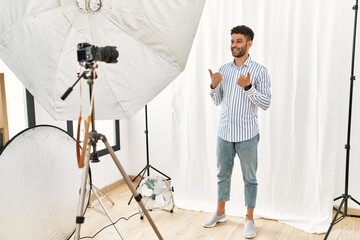 Sticker - Arab young man posing as model at photography studio success sign doing positive gesture with hand, thumbs up smiling and happy. cheerful expression and winner gesture.