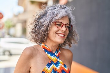 Wall Mural - Middle age grey-haired woman smiling confident wearing glasses at street