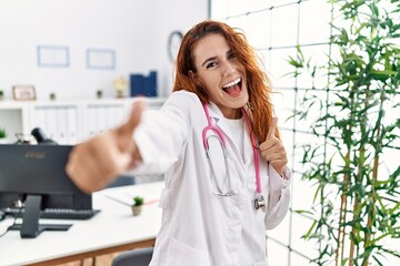 Sticker - Young redhead woman wearing doctor uniform and stethoscope at the clinic approving doing positive gesture with hand, thumbs up smiling and happy for success. winner gesture.