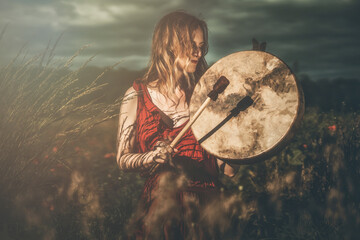 beautiful shamanic girl playing on shaman frame drum in the nature.