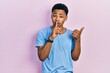 © Krakenimages.com - Young african american man wearing casual blue t shirt asking to be quiet with finger on lips pointing with hand to the side. silence and secret concept.