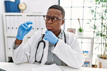 Young african doctor man holding syringe at the hospital thinking worried about a question, concerned and nervous with hand on chin