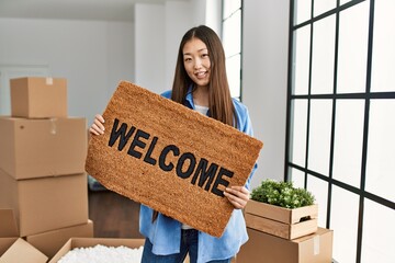 Sticker - Young chinese girl smiling happy holding welcome doormat at new home