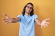© Krakenimages.com - Young hispanic man standing over yellow background looking at the camera smiling with open arms for hug. cheerful expression embracing happiness.