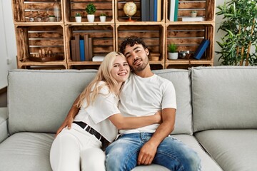 Wall Mural - Young beautiful couple sitting on the sofa and hugging at home.