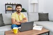 © Krakenimages.com - Young man with beard using laptop at home skeptic and nervous, disapproving expression on face with crossed arms. negative person.