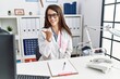 © Krakenimages.com - Young doctor woman wearing doctor uniform and stethoscope at the clinic smiling with happy face looking and pointing to the side with thumb up.